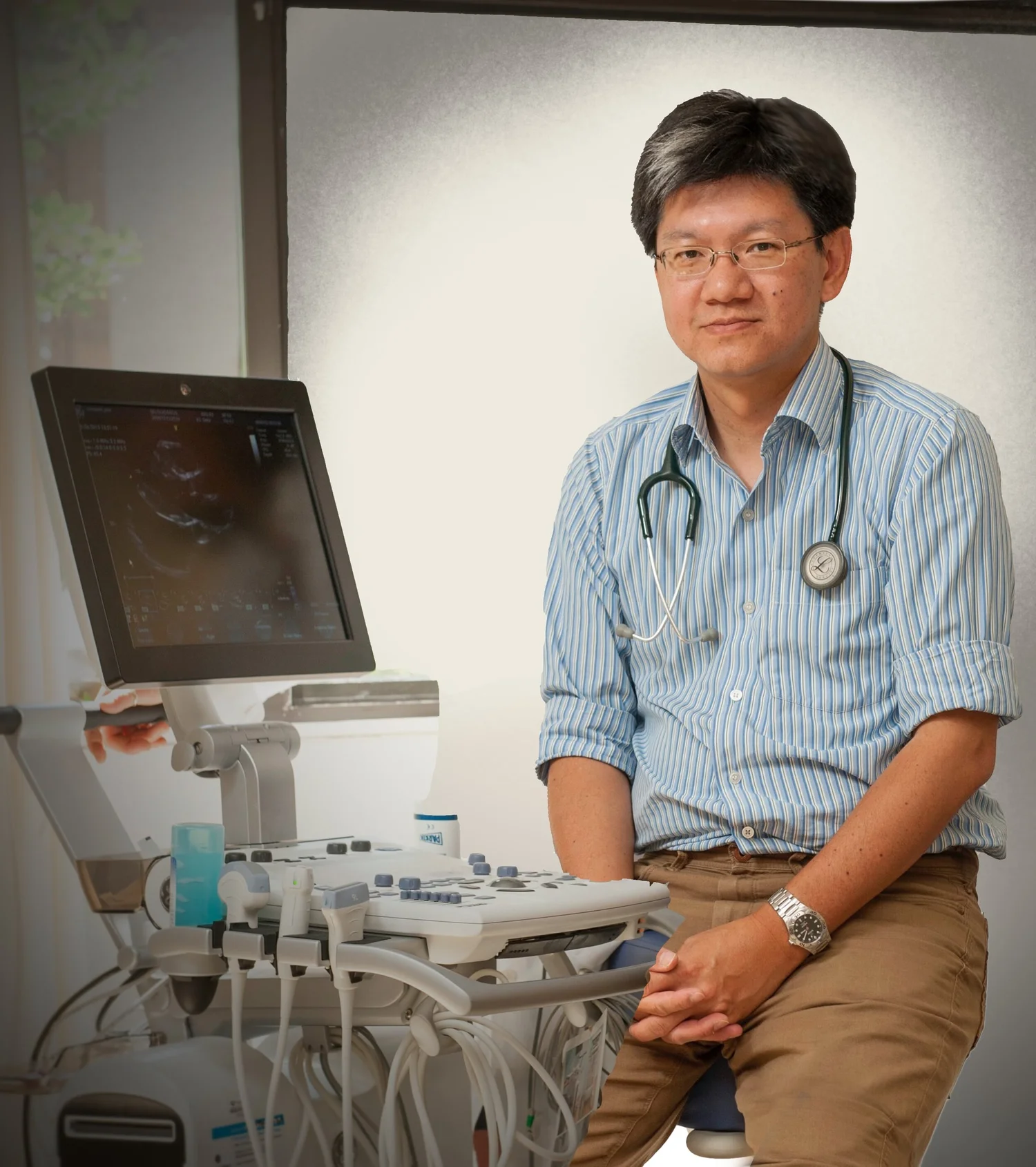 Dr. Robert Y. Shaw, MD FRCPC, seated beside an ultrasound machine wearing a light blue striped shirt and stethoscope
